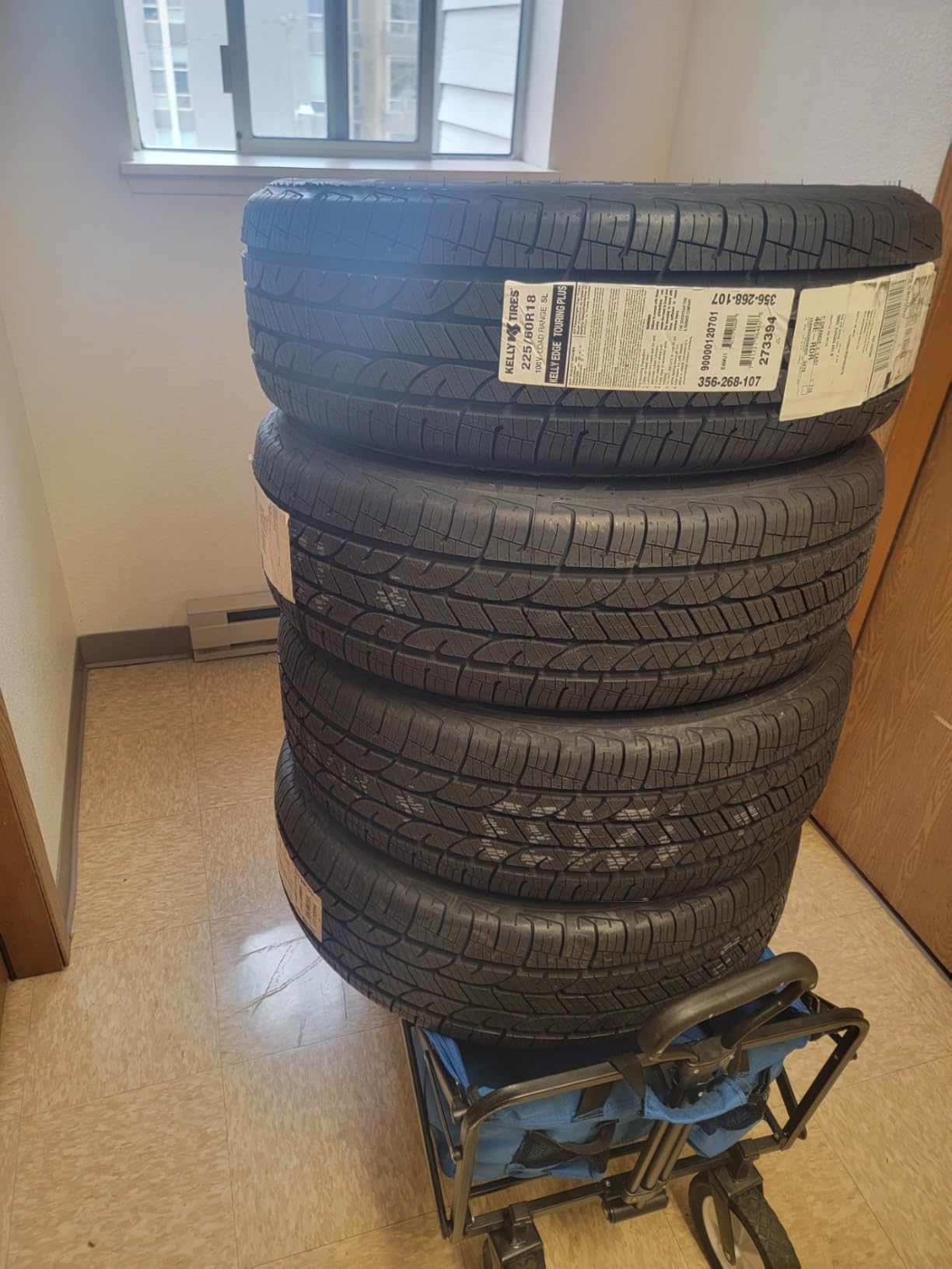 Four new Kelly Edge Touring Plus tires stacked indoors, factory label facing the camera